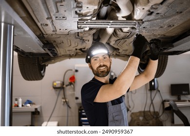 Mechanic smiling while wearing headlamp and repairing car in auto repair shop. Person ensures vehicle maintenance and safety while working in professional environment. - Powered by Shutterstock