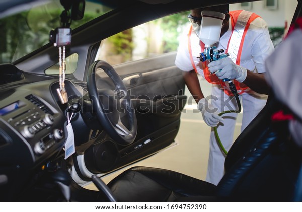 Mechanic spraying to kill the Covid-19\
in the car that can kill the virus in the car. Mechanic wearing a\
protective mask and spraying aerosol or virus in the\
car.
