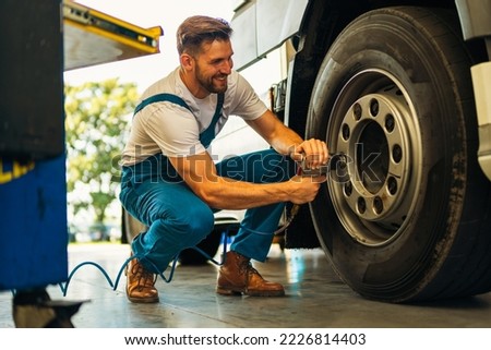 The mechanic squats next to the wheel of the truck and tightens the wheel screws. Use special tools. Car mechanic in the workshop
