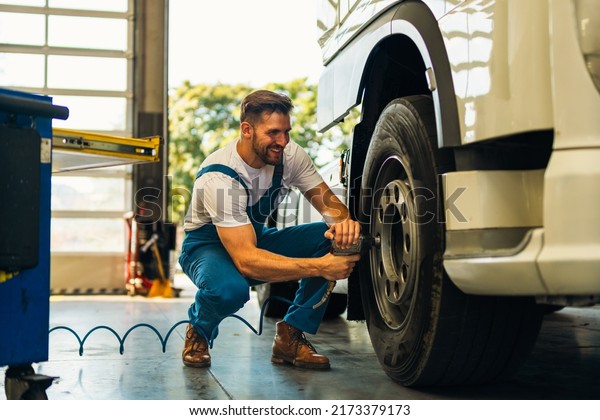 The mechanic squats next to the wheel of the\
truck and tightens the wheel screws. Use special tools. Car\
mechanic in the workshop