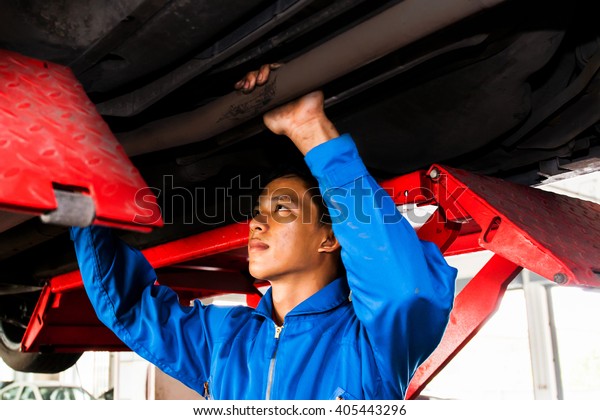 Mechanic standing and fixing under a lifted car\
with copy space