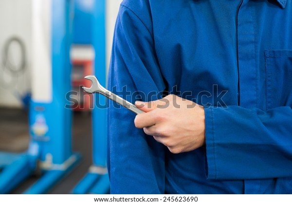 Mechanic standing with wrench in hand at the\
repair garage