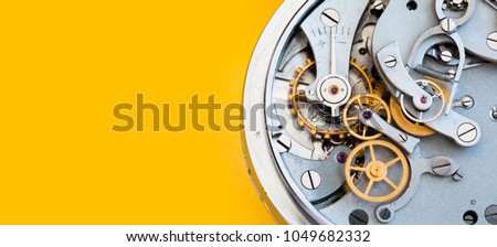 Mechanic stopwatch chronometer mechanism, spring bronze cogs wheels macro view. Shallow depth of field, selective focus. Yellow colorful background. Copy space.