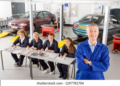 Mechanik mit Studierenden, die den Automobilhandel in der Universitätsgarage studieren und bei der Kamera lächeln