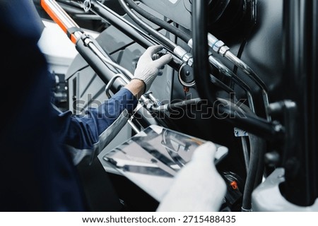 Mechanic with tablet computer control and fix problem of hydraulic hoses from industrial mining truck.