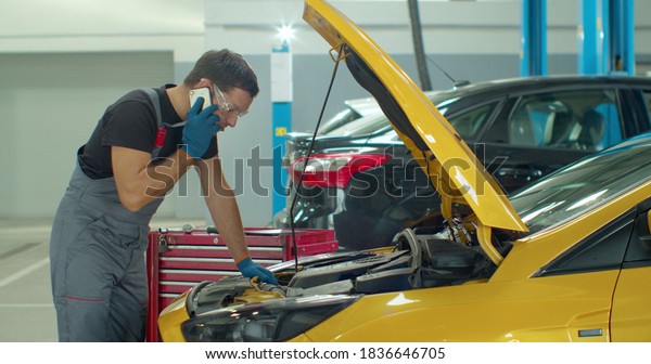 Mechanic talking on a mobile phone with the\
car owner while repairing a car in a\
garage.