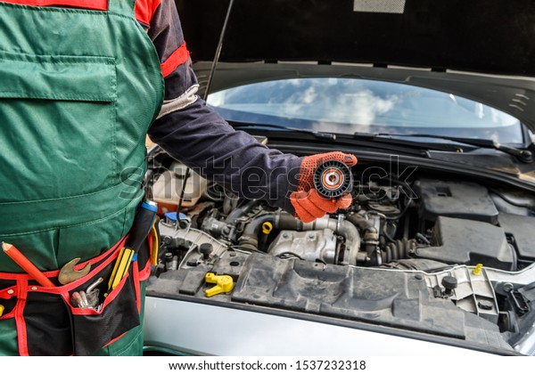 Mechanic with tool belt showing car filter against car\
engine close up