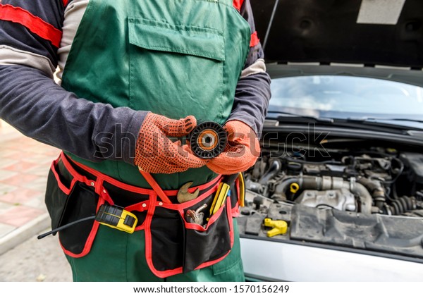 Mechanic with tool belt showing car filter against car\
engine close up
