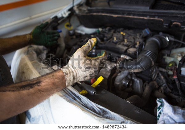 Mechanic with a\
tool in his hands repairing the motor of the machine. The process\
of working in the service\
station