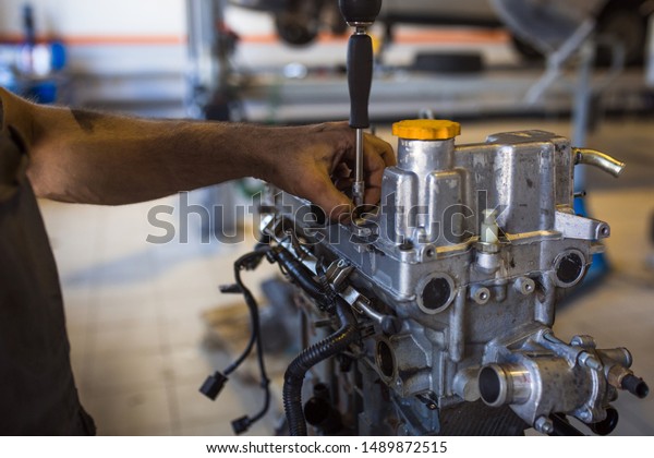 Mechanic with a\
tool in his hands repairing the motor of the machine. The process\
of working in the service\
station