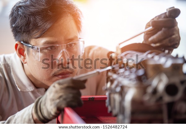 Mechanic with a tool in his hands repairing the motor of\
the machine. 
