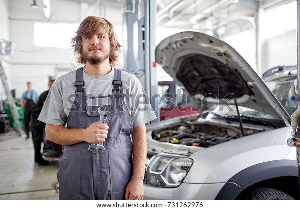 Mechanic\
with tools on the background of the open\
hood