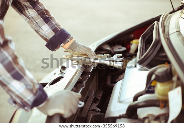 Mechanic with tools\
repairing car. Male hand in glove with the adjustable wrench and\
open the hood of the\
car.