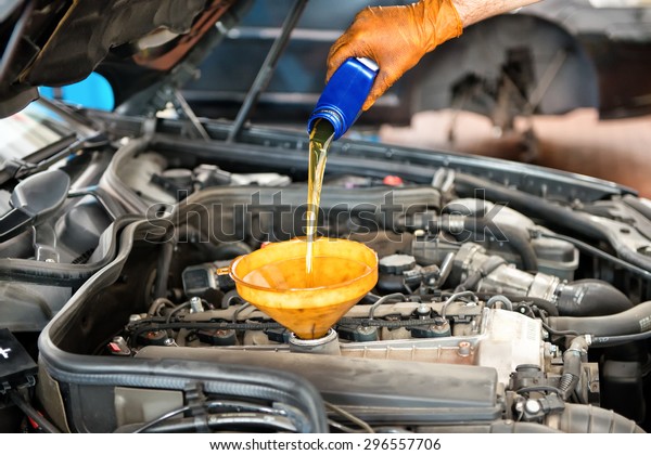 Mechanic topping up the oil in a car pouring a pint\
of oil through a funnel into the engine, close up of his hand and\
the oil
