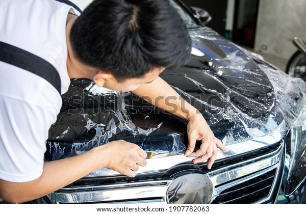 Mechanic with transparent film, car paint\
protection. Mechanic installs car paint protection film. Install\
car paint protection film. Car wrap\
concept.