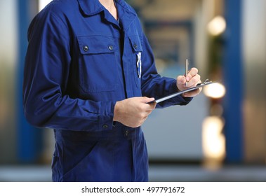 Mechanic in uniform with a clipboard and pen on gas station blurred background