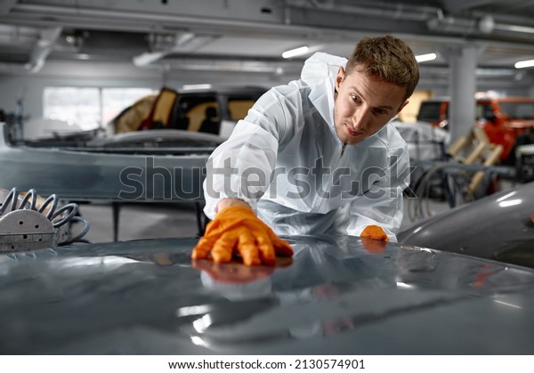 Mechanic in uniform\
sanding painted car\
body