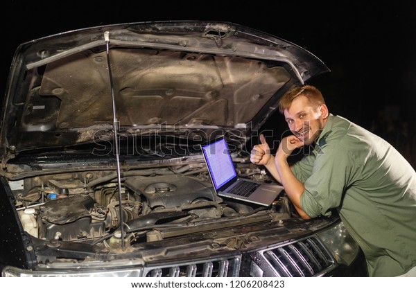 The mechanic in uniform shows that the engine is all\
right. Raised thumbs up. the laptop connects to the car for\
inspection and adjustment. Mechanic carries out maintenance of the\
car.