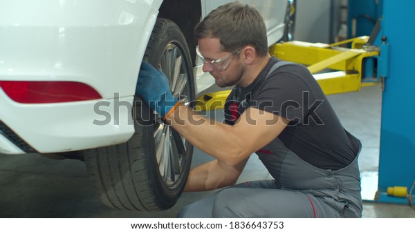 Mechanic is unscrewing lug nuts with a pneumatic\
impact wrench. Specialists removes the wheel in order to fix a\
component on a\
vehicle.