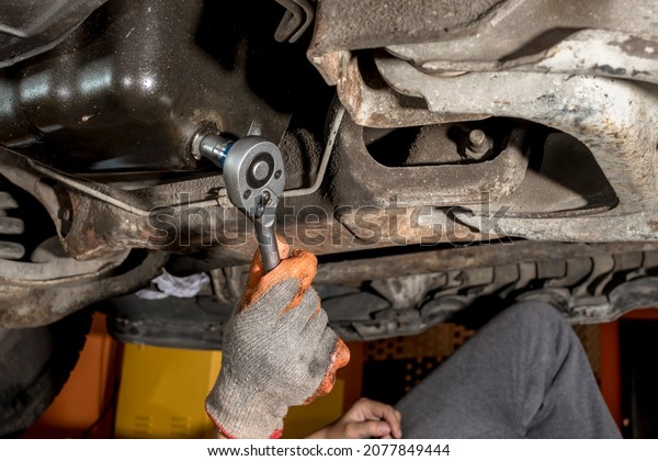 A mechanic unscrews an oil drain plug
underneath the chassis of a SUV with a ratchet wrench. First step
of an oil change. Maintenance
procedure.