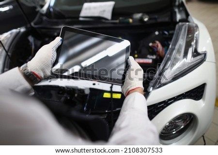 Mechanic use tablet device with black screen in front of car.