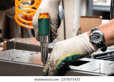 A mechanic uses a pneumatic rivet gun to install a rivet onto an aluminum sheet. The work of the pneumatic riveting gun