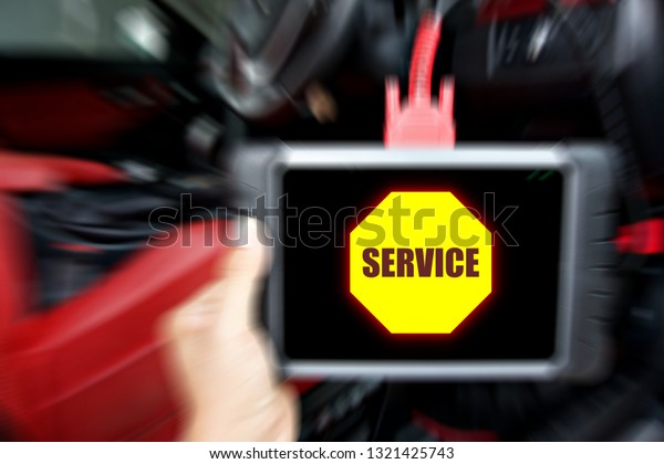 Mechanic is using a car diagnostic tools\
servicing a car in selective focus. Car diagnostic tools with\
yellow service massage on\
screen\
