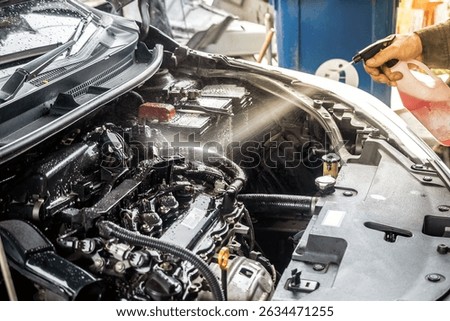 The mechanic is using a cleaning spray to clean the engine compartment.