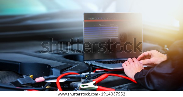 Mechanic using computer for diagnostics\
engine. On screen running automobile software. Repairing car. Blur\
garage auto repair service in\
background.\

