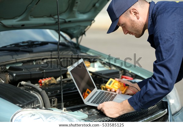 Mechanic\
using computer diagnostics while repairing\
car
