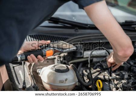 Mechanic using diagnostic tool to inspect car engine during vehicle maintenance