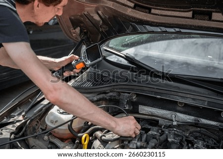 Mechanic using diagnostic tool to inspect car engine during vehicle maintenance