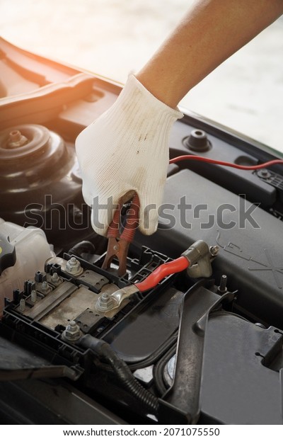 Mechanic is using electric car battery charger\
through jumper\
wires.\
