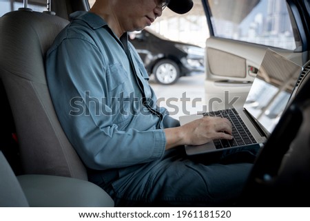 Mechanic using laptop computer to check during work a car engine on car at repair garage. 
