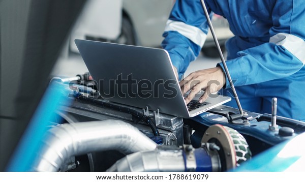 Mechanic using\
laptop computer working tuning on car for the efficiency of the\
race car in garage.maintenance\
concept