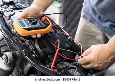 mechanic using multimeter to check the voltage level on motorcycle battery at motorcycle garage, Maintenance and repair concept - Shutterstock ID 1848994642