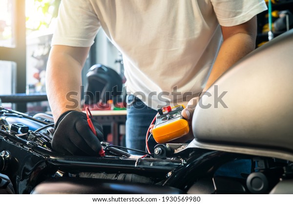 mechanic using multimeter to check the voltage\
level on motorcycle battery at motorcycle garage, Maintenance and\
repair concept