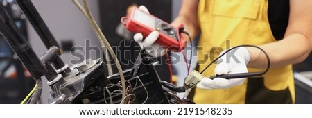 Mechanic using multimeter checks voltage level on motorcycle battery in motorcycle garage. Maintenance and repair concept
