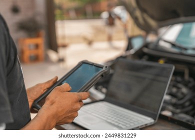 Mechanic using tablet and laptop to repair a car in a rural garage - Powered by Shutterstock