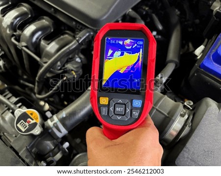 Mechanic using thermal imaging camera inspecting car engine for overheating issues