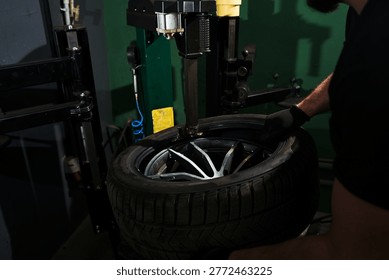 Mechanic using tire changer machine to mount rubber tire onto dark alloy rim close-up