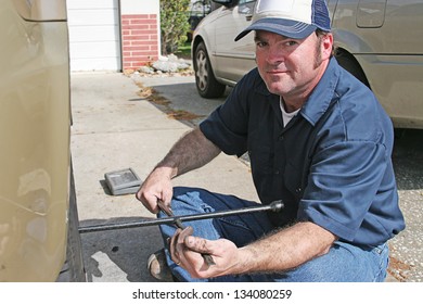Mechanic using a tire iron to remove lug nuts from an automobile tire.