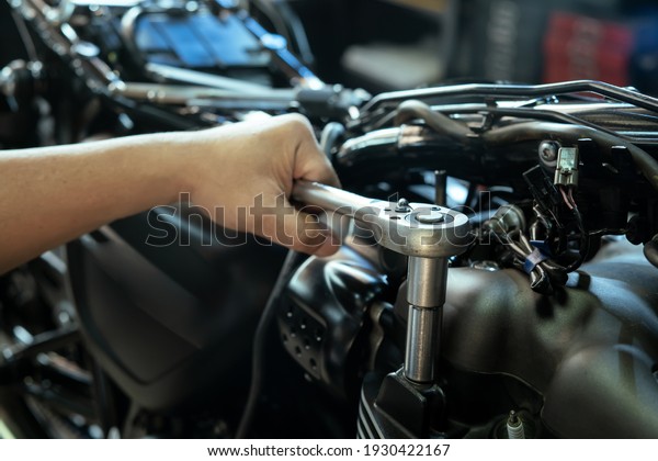 Mechanic using a wrench and socket on cylinder head\
of a motorcycle .maintenance,repair motorcycle concept in garage\
.selective focus