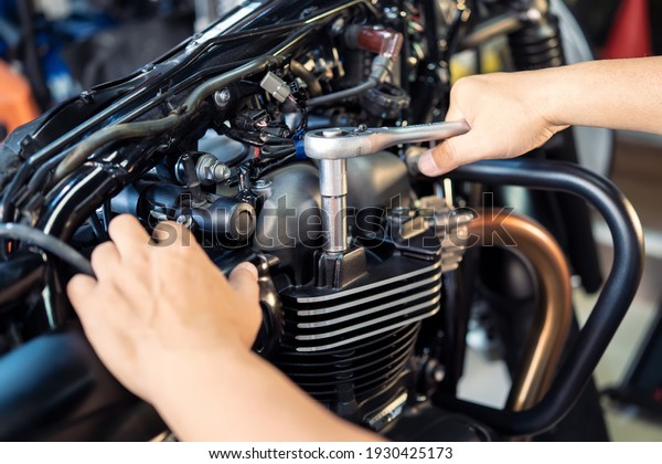 Mechanic using a wrench and socket on cylinder head\
of a motorcycle .maintenance,repair motorcycle concept in garage\
.selective focus