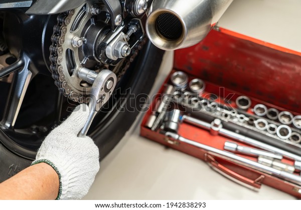Mechanic using a wrench and socket on motorcycle\
sprocket   .maintenance and repair concept in motorcycle garage\
.selective focus 