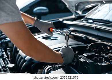 Mechanic using wrench while working on car engine at garage workshop, Car auto services and maintenance check concept.