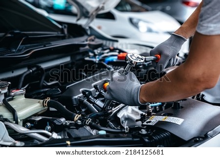 Mechanic using wrench while working on car engine at garage workshop, Car auto services and maintenance check concept.