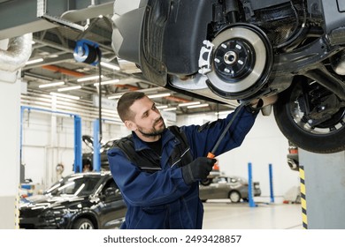 A mechanic wearing gloves inspects the undercarriage of a car lifted on a hoist in an auto repair shop - Powered by Shutterstock