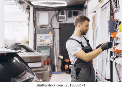 Mechanic wearing gloves organizing tools on a wall rack in a garage workshop. Focused on efficiency in a professional automotive repair setting. - Powered by Shutterstock