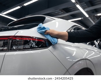 A mechanic wipes the body of a white car with a microfiber cloth.  - Powered by Shutterstock